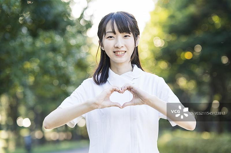 穿着白色衣服的女人用双手做出心形。图片素材