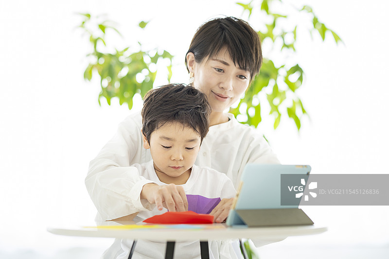 父母和孩子们一边看着平板电脑一边折纸图片素材