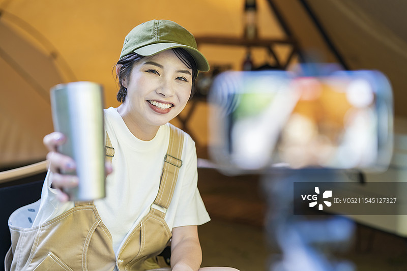 年轻女性露营者在帐篷里用智能手机拍照图片素材