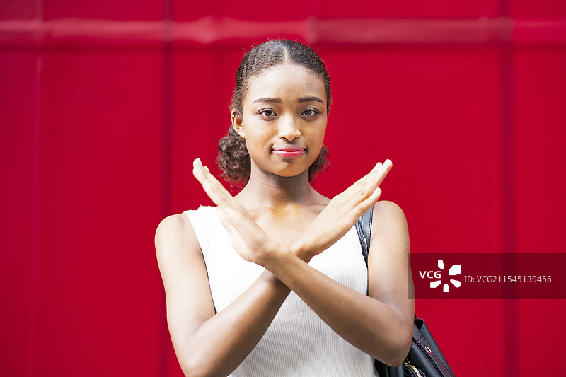 年轻女商人在红色墙壁前做出“NG”手势图片素材