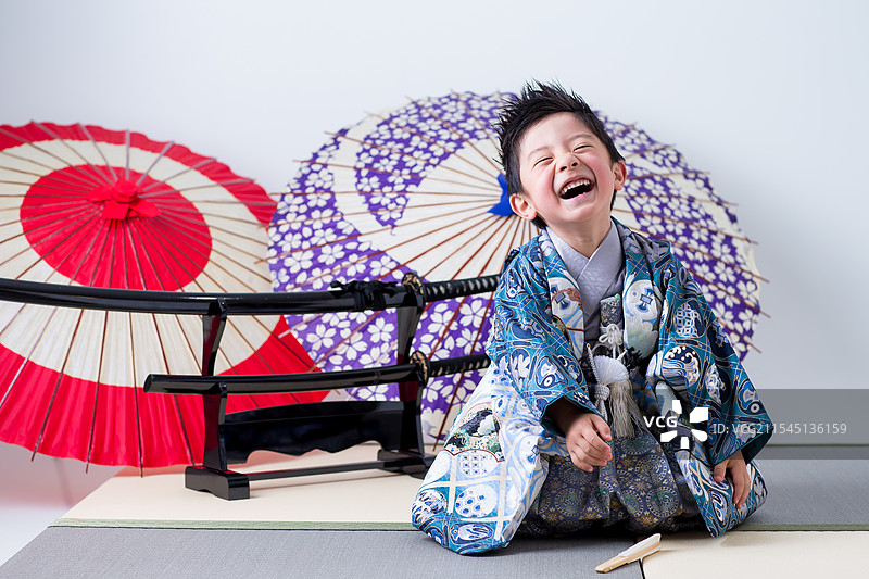 穿着和服的男孩坐在榻榻米上，手持剑。图片素材