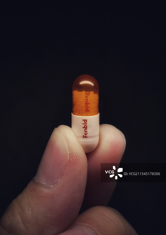 沧桑手指捏住举起一粒止疼药芬必得胶囊的特写救命图片素材