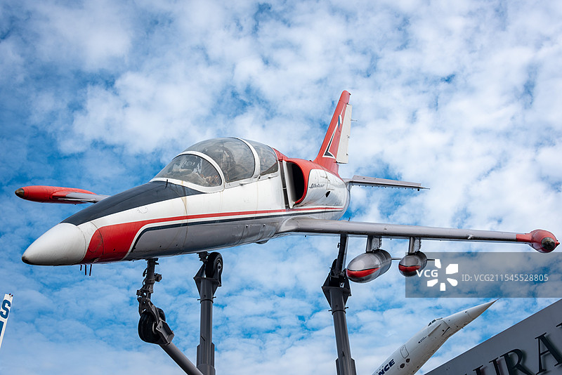 一架红白相间的飞机在蓝天背景下停驻，驾驶舱透明展示内部细节，尾翼红白标志醒目图片素材