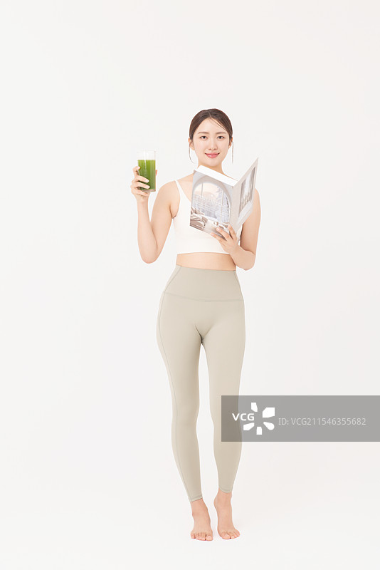 穿着运动服的年轻女性，喝着健康饮品并阅读书籍的肖像图片素材