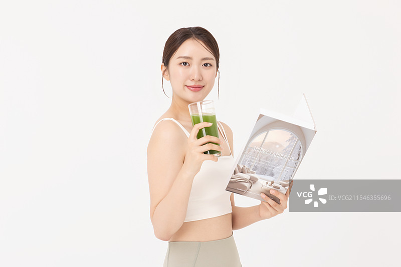 穿着运动服的年轻女性，喝着健康饮品并阅读书籍的肖像图片素材