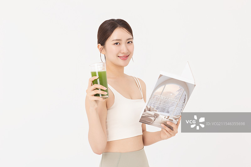 年轻女性穿着运动服，喝着健康饮品并阅读书籍的肖像图片素材