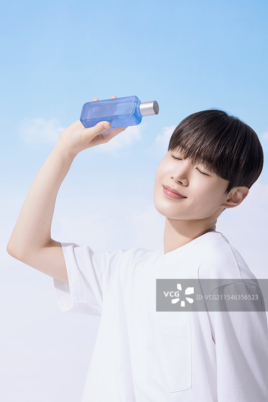 年轻男子手持基础化妆品，背景是云朵。图片素材