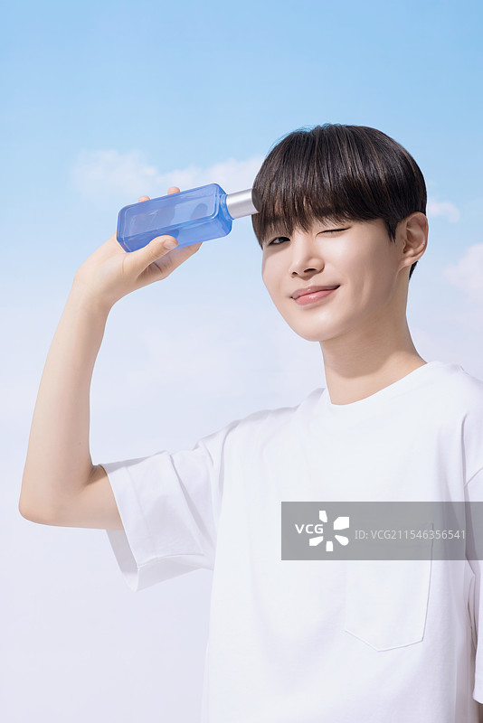 年轻男子手持基础化妆品，背景是云朵。图片素材