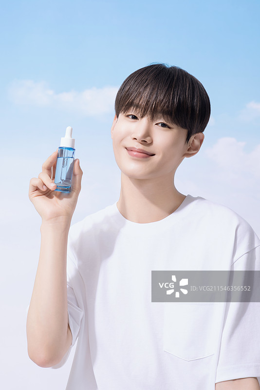 年轻男子手持基础化妆品，背景是云朵。图片素材