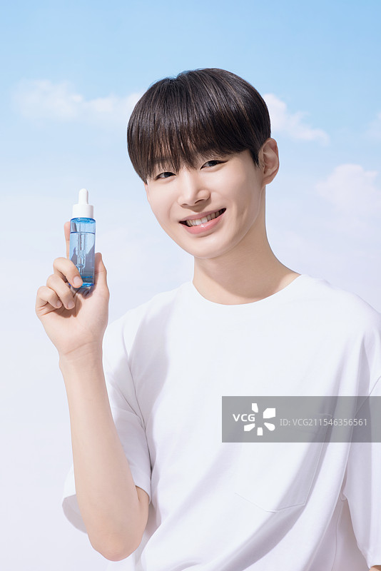 年轻男子手持基础化妆品，背景是云朵。图片素材