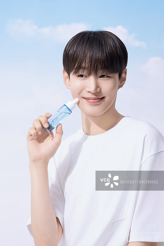 年轻男子手持基础化妆品，背景是云朵。图片素材