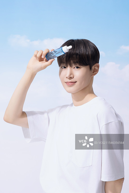 年轻男子手持基础化妆品，背景是云朵。图片素材