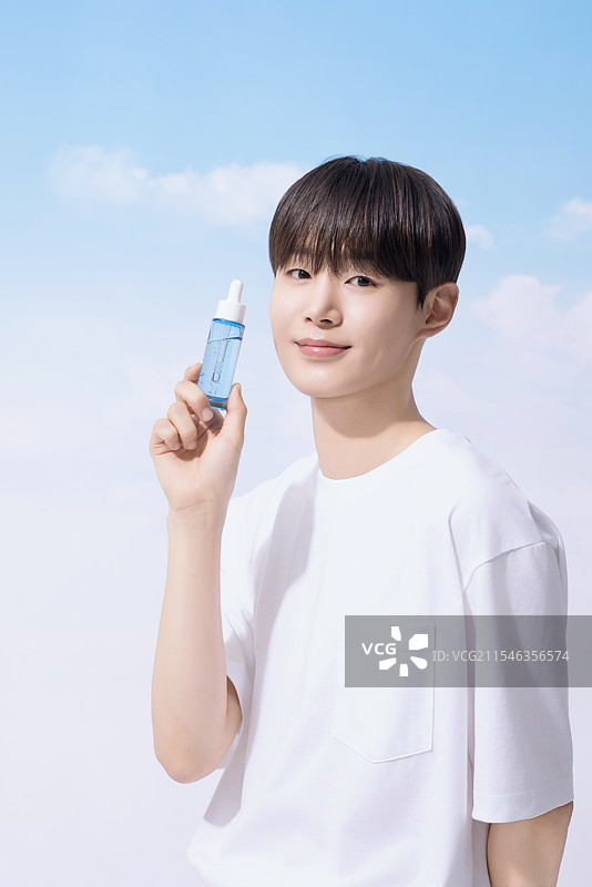 年轻男子手持基础化妆品，背景是云朵。图片素材