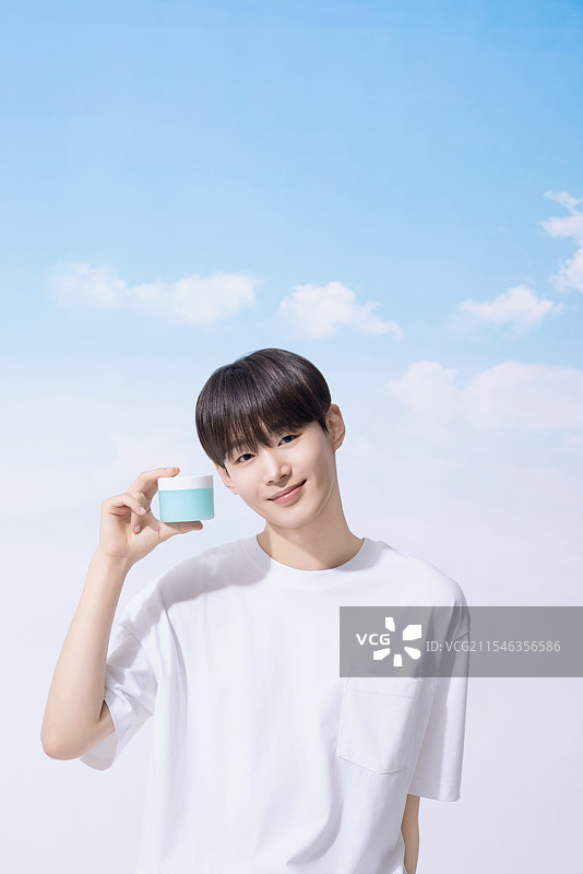 年轻男子手持基础化妆品，背景是云朵。图片素材