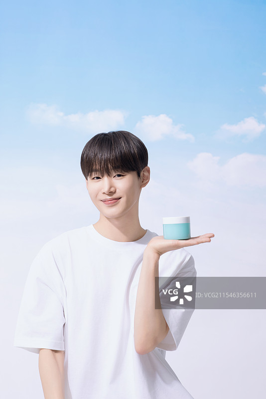 年轻男子手持基础化妆品，背景是云朵。图片素材