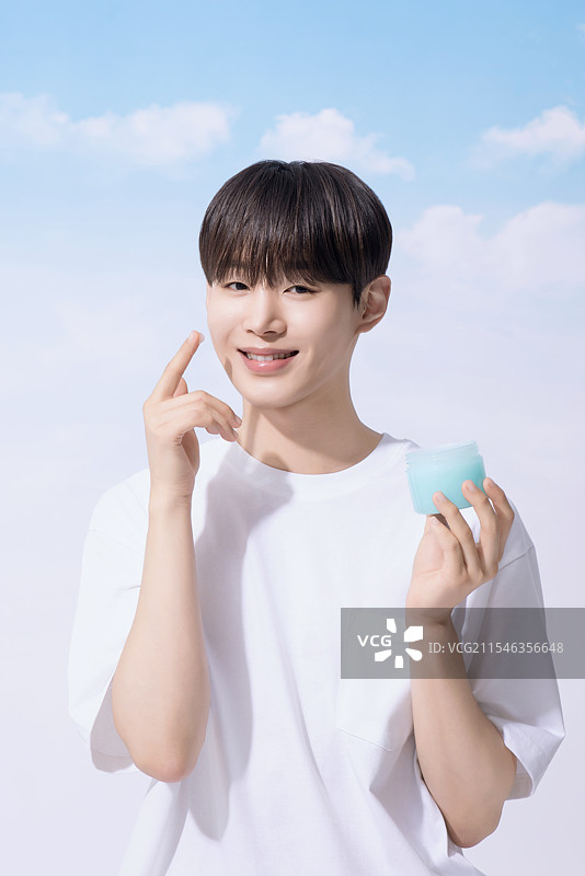 年轻男子手持基础化妆品，背景是云朵。图片素材