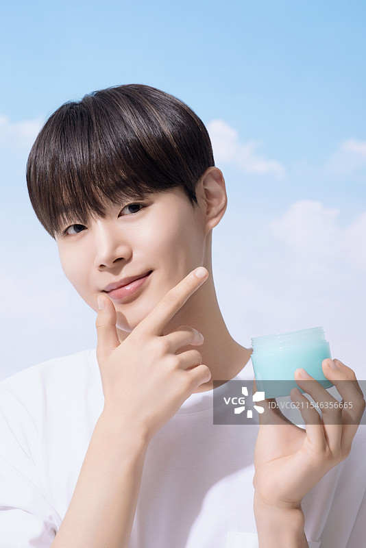 年轻男子手持基础化妆品，背景是云朵。图片素材