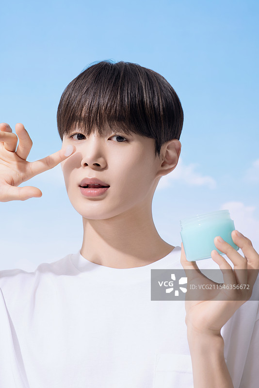 年轻男子手持基础化妆品，背景是云朵。图片素材