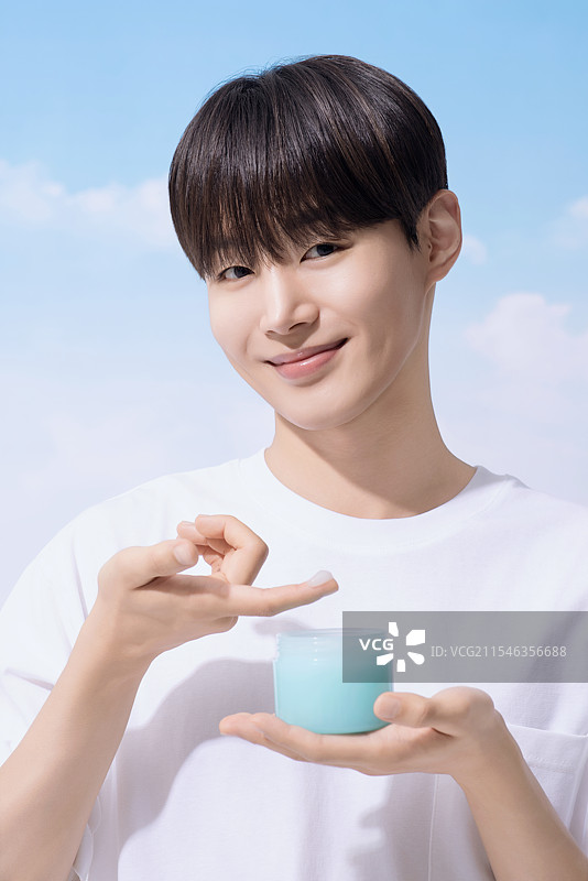 年轻男子手持基础化妆品，背景是云朵。图片素材