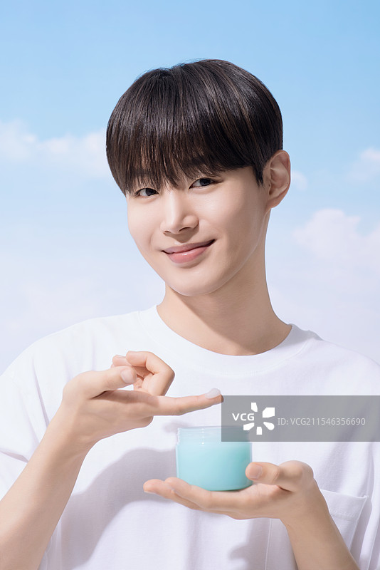年轻男子手持基础化妆品，背景是云朵。图片素材
