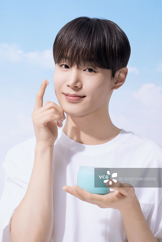 年轻男子手持基础化妆品，背景是云朵。图片素材