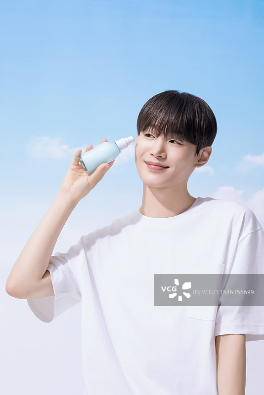 年轻男子手持基础化妆品，背景是云朵。图片素材