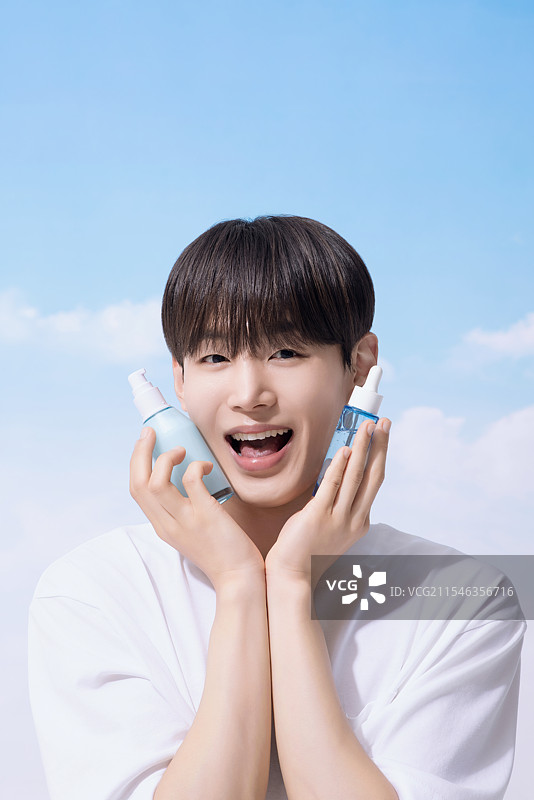 年轻男子手持基础化妆品，背景是云朵。图片素材