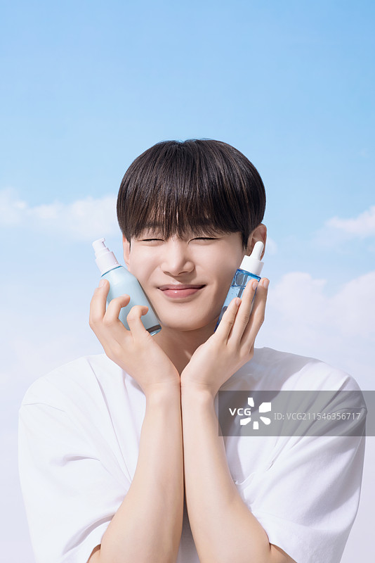 年轻男子手持基础化妆品，背景是云朵。图片素材