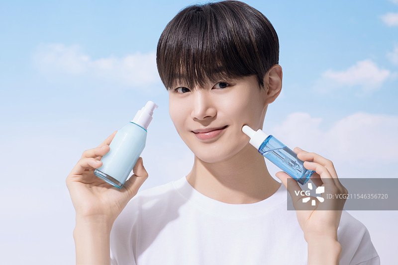 年轻男子手持基础化妆品，背景是云朵。图片素材
