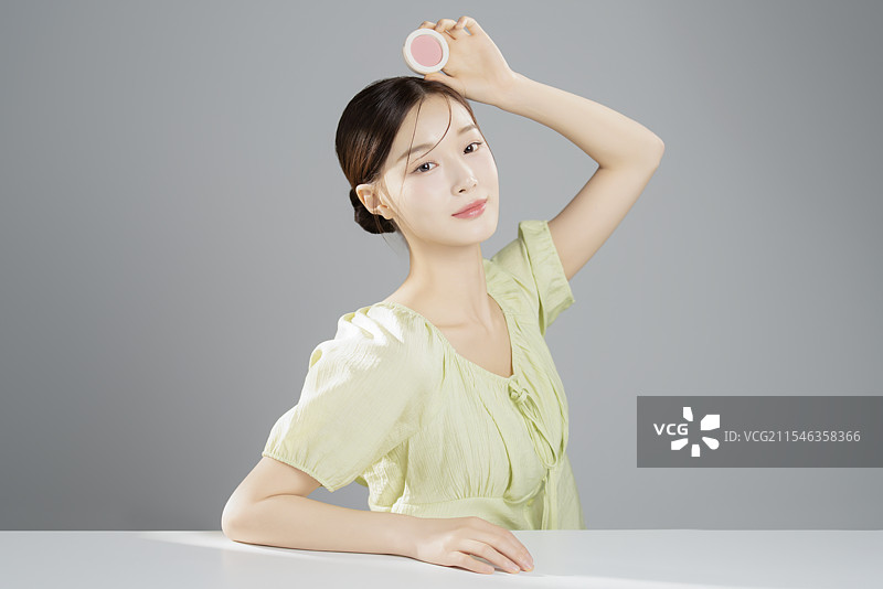 一位穿着鲜艳衣服的20多岁漂亮女性，坐着摆姿势与化妆品合影图片素材