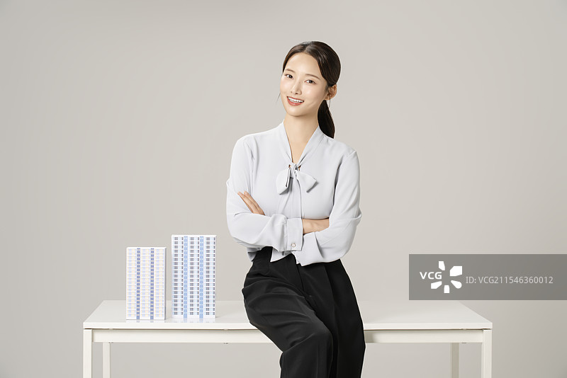 一位20多岁的年轻女性坐在桌子旁，桌上摆放着公寓模型。图片素材