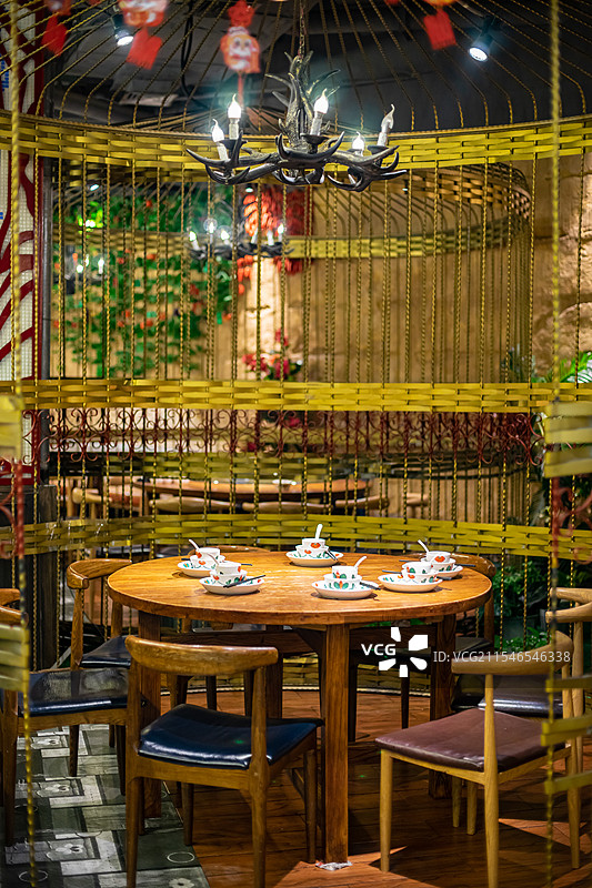 中国餐饮餐厅饭店饭馆行业，空的餐桌拍摄主题，巨大的铁质鸟笼里木制圆桌上的餐具，室内无人图像摄影图片素材