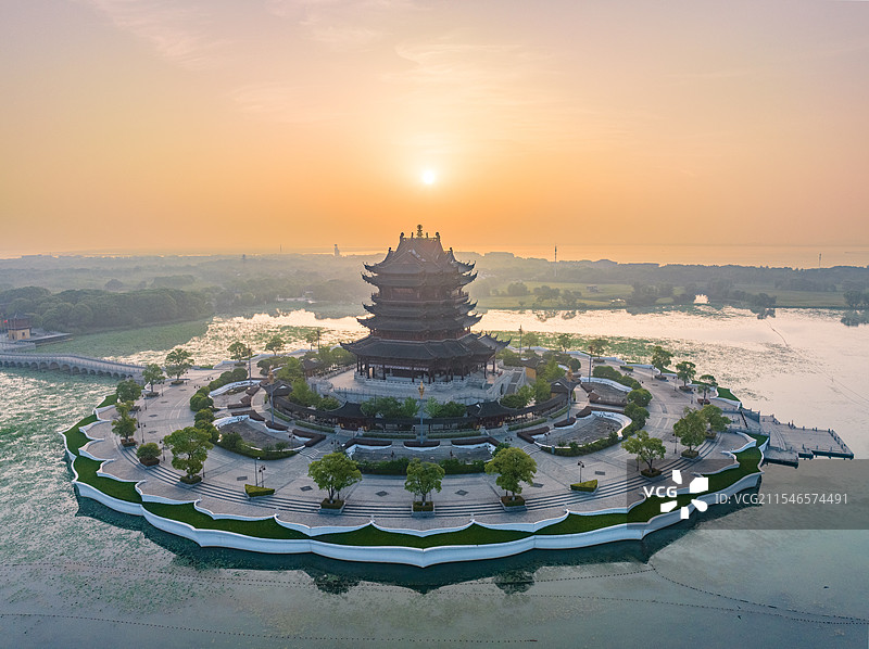 湖心岛上的中国风格建筑，环绕绿树草坪，夕阳余晖映照，温暖而神秘。图片素材