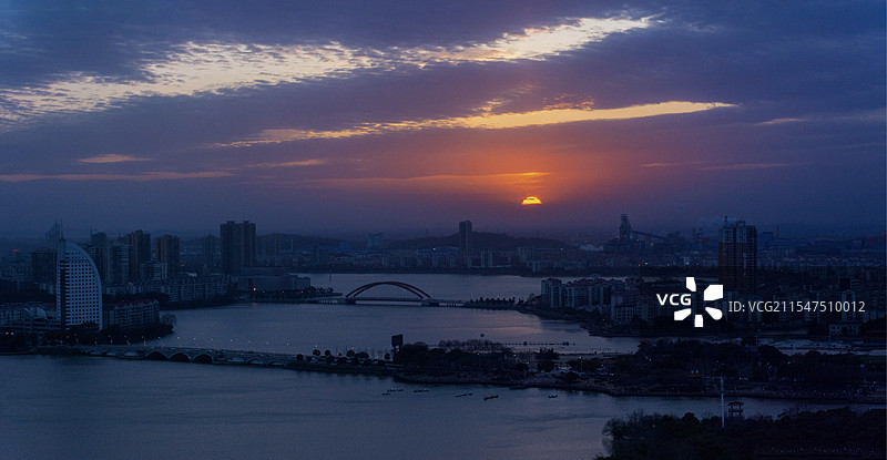 鄂州鄂城区的黄昏景象，夕阳于天际散发柔和光芒，洒在城市建筑群与宽阔的水面上。图片素材