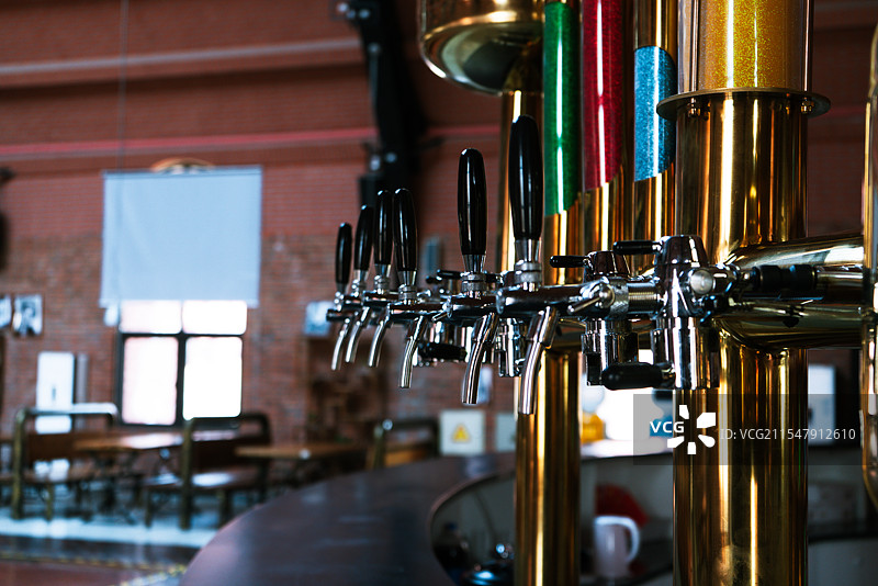 金属啤酒龙头排列于吧台，背景红砖墙，凸显酒吧的工业风氛围。图片素材