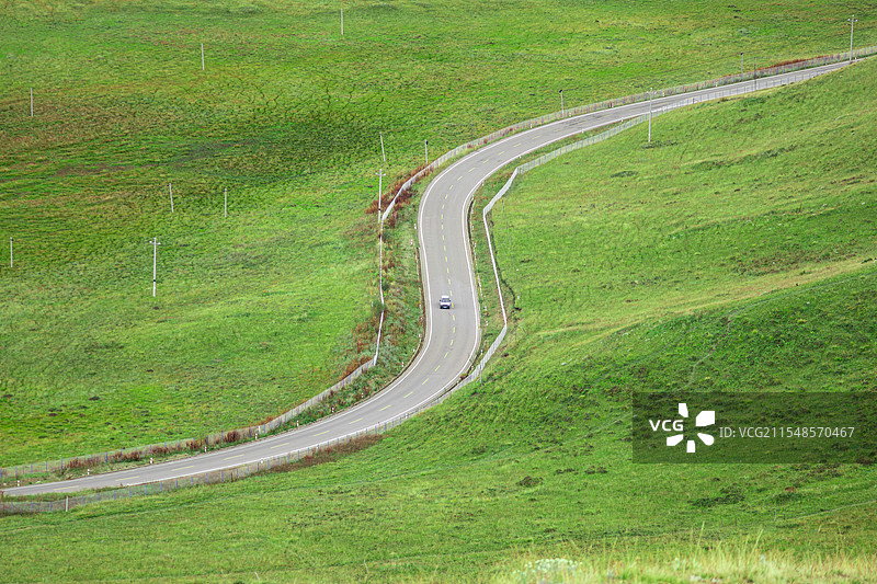 小汽车行驶在绿色草原中的公路上图片素材