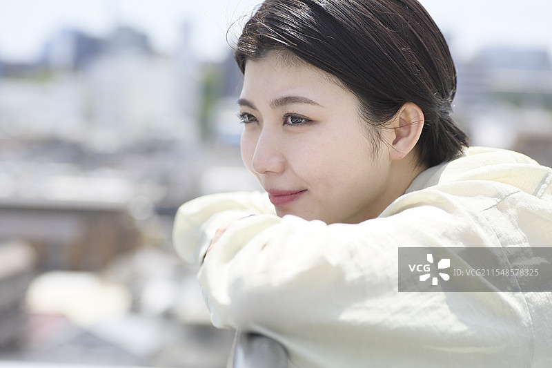 微笑的年轻女性靠在栅栏上，双肘支撑着。图片素材