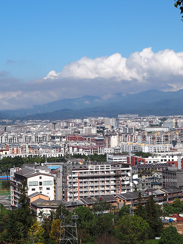 2024年11月10日云南普洱市梅子湖公园山顶遥望茶山和普洱市区在蓝天白云下的自然与现代建筑景观图片素材