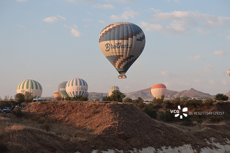 土耳其卡帕多西亚日出时分的热气球在喀斯特地貌的群山中穿行上升图片素材