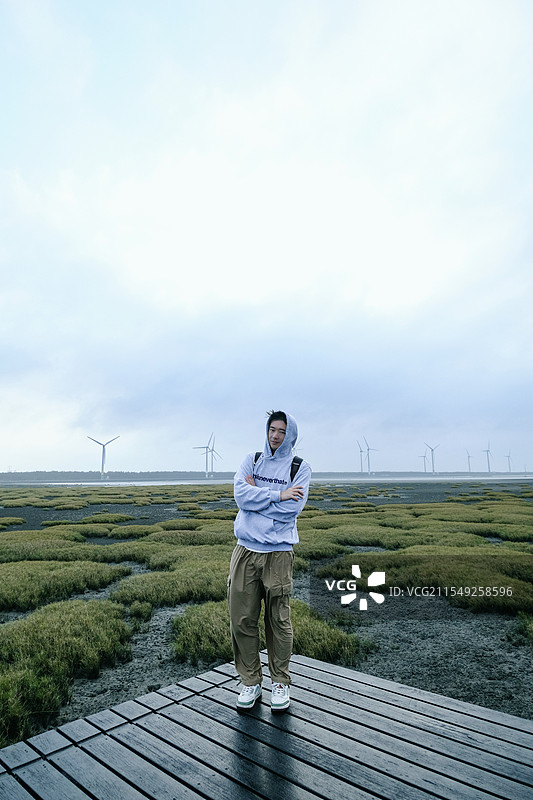 站在高美湿地步道上穿着帽衫双臂交叉的男子图片素材