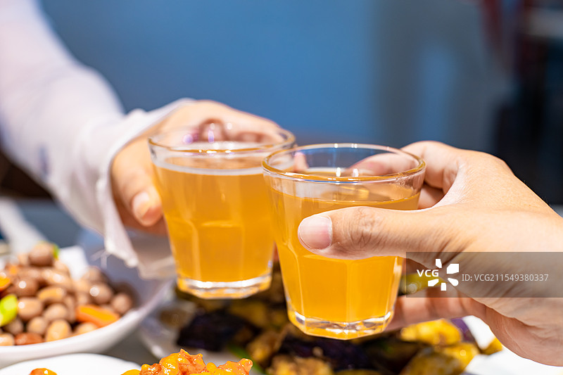 中国餐饮行业饮食产业，传统经典中国食品，饭桌上的两个端着啤酒干杯碰杯交杯，室内无人图像图片素材