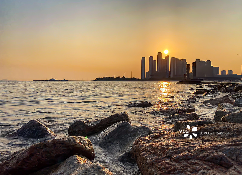 前景礁石远景摩天大楼的深圳人才公园日落景色图片素材