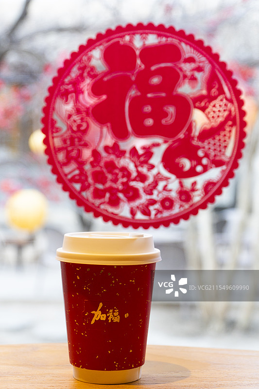 有“加福”两个字的纸杯在福字窗花前面图片素材