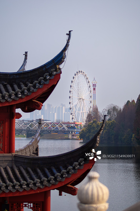 吉安中式翘角屋檐的建筑近在眼前，远处湖面上桥梁横跨，摩天轮矗立在城市建筑群间。图片素材