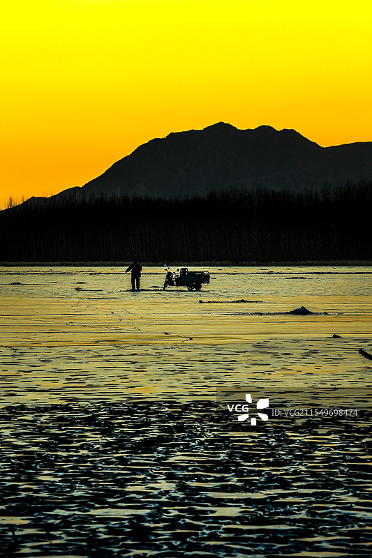 冬季夕阳下，北京妫水河冰面上的钓鱼人图片素材
