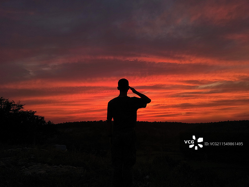 男子在绚丽晚霞中敬礼的剪影画面图片素材