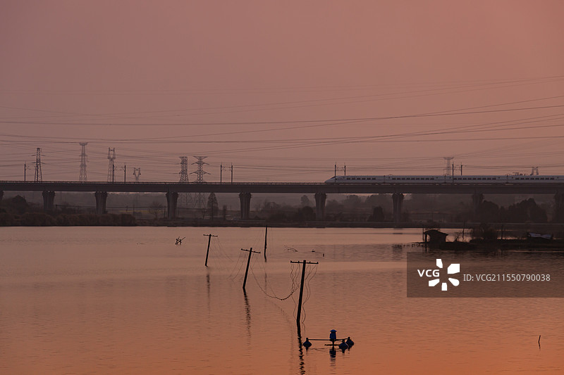 日落时分在夕阳下湖水上高架桥飞驰的高铁图片素材