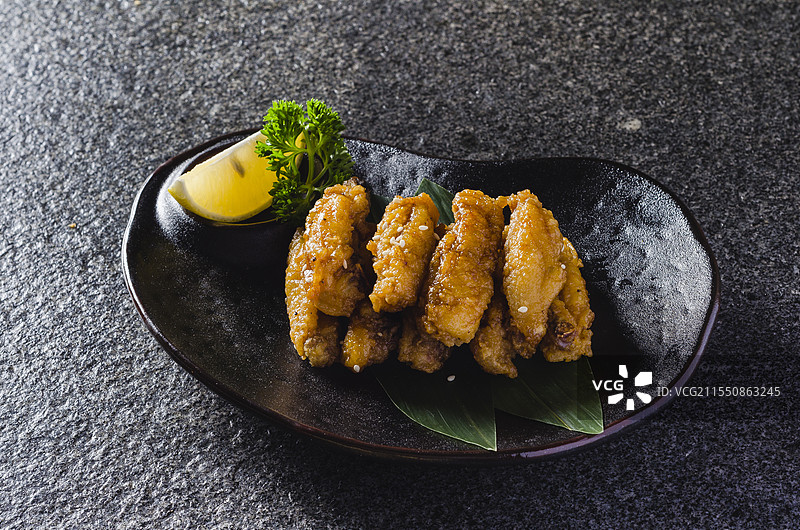 一盘色泽诱人的日式炸鸡翅，整齐摆放于黑色餐盘，点缀柠檬与欧芹，散发浓郁日式风味。图片素材