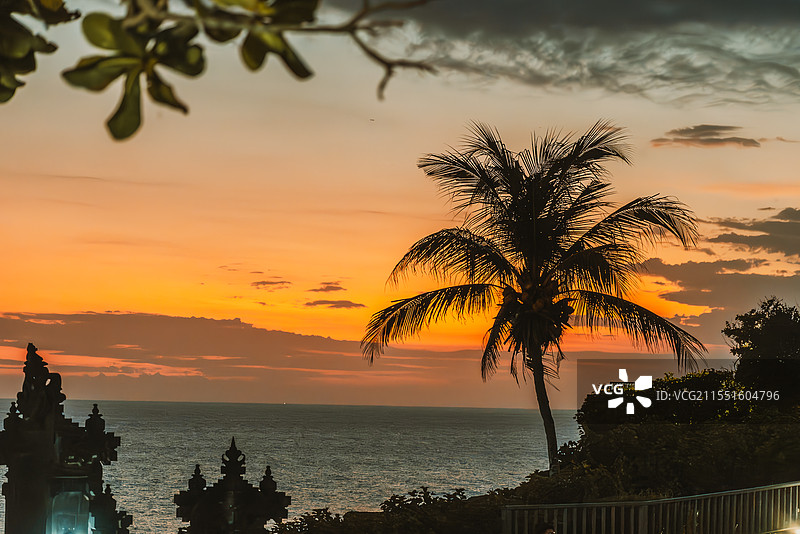 晴朗的黄昏，印度尼西亚巴厘岛海神庙，落日余晖映红天际，一棵椰树的剪影在微弱的光线下图片素材