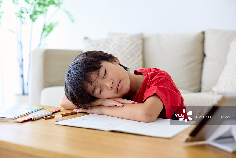 一个年轻男孩趴在桌子上睡觉，头靠在桌子上图片素材